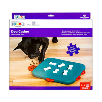 Nina Ottosson Hound Dog Casino puzzle toy in its retail packaging, featuring a teal board with white bone-shaped treats and red handles, shown on a white background.