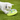 A small white dog on green grass interacting with a Nina Ottosson Wobble Bowl with a lime-green base, and translucent top with a blue centre.