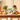 A dog sits at a wooden dining table looking at a box of Forthglade dog food, surrounded by fresh vegetables and ingredients.