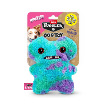 A Fuggler Bonkers dog toy shaped like a monster, shown both inside its retail packaging and unpacked. The plush toy is turquoise blue with purple patches, featuring large black eyes, a wide grin with white teeth, and a pink Bonkers tag attached near the bottom left.