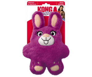 White background with a KONG Snuzzles Bunny dog toy, the main body is made from purple fur body with pink feet and inner ears with stitched features attached to a cardboard backing.