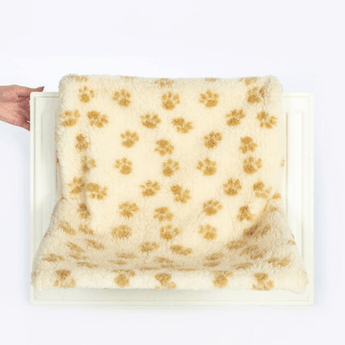 White background with a white radiator shown with a hand touch the side of it, on the radiator is a cream radiator cat bed with brown pawprints.