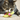 Brown tabby cat with a white nose and paws playing with green, pink and yellow Hummingbird cat toy with a three curls of ribbon as tail on carpet.
