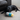 Young black Labrador with rocket dog toy with yellow top, blue middle, grey wings and bottom with multicoloured stars in it's mouth. Lying on cream carpet with a brown leather sofa in the background.