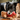 Black and white collie-type dog with a brown bear plush dog toy with red fabric with stars waist coat and red and white stripy trousers, a brown nose with stitched eye details, pictured in a living room with a Christmas tree and presents in the back ground.