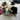 A black and white cat playing with an Ancol plush cat-shaped toy dressed as a bandit with a black-and-white striped shirt and a white bank box, on a living room carpet.
