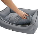 White background with a hand lifting the corner of the cushion off a bolster-type grey dog bed to show the underside. 