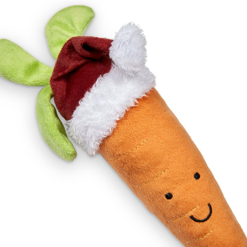 White background with a close up of a plush toy carrot with a red Santa hat and stitched eyes and smile. 