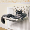Wallpapered room with a white radiator, pictured with a long haired brown tabby cat on a cream radiator cat bed with brown pawprints. 