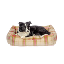 Black and white collie dog lying on a bolster red and green checked dog bed pictured on a white background. 