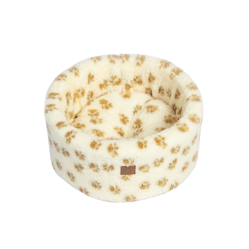 White background with a round cream cat bed with brown pawprints. 