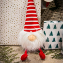 Christmas presents with a Gonk plush dog toy with red and white stripy hat and red rope legs, with a white beard and white bobble on the hat , sat in the foreground.