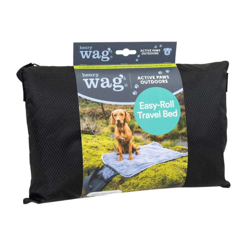 Henry Wag Easy-roll travel bed packed up in black bag in a cardboard sleeve with text 'Henry Wag, Active Paws Outdoors, Easy-roll Travel Bed' with a picture of a red Labrador dog lying on the mat. Pictured on a white background. 