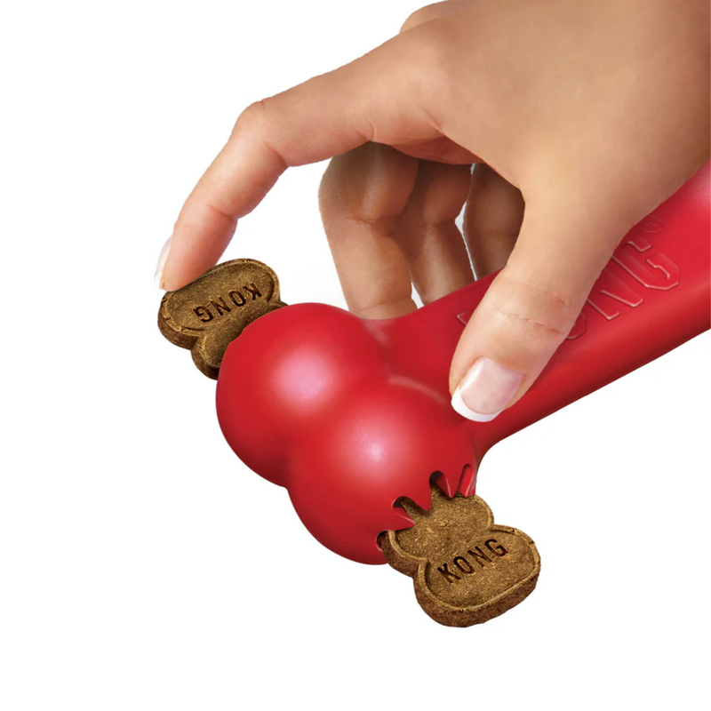 White background with a hand inserting a KONG Goodie treat into a KONG red bone. 