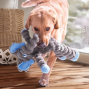 Yellow Labrador with a grey soft fabric and rope Elephant KONG Dog Toy with a blue ears, eyes and feet in the dog's mouth, pictured in a living room with wooden floors.