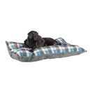 Black adult Labrador lying on a pillow-type blue checked dog bed with a grey underside pictured on a white background. 