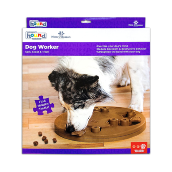 Nina Ottosson Dog Worker puzzle toy in its retail packaging, featuring a tan interactive treat-dispensing board with pale green rings and a photo of a dog using the toy.