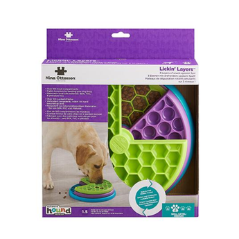 Nina Ottosson Lickin' Layers dog lick toy in its original retail packaging, featuring a tri-colour design of lime green, purple, and blue, with a picture of a dog licking the toy on the box.