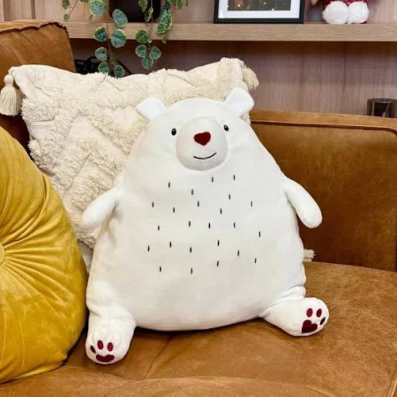 Side view of white polar bear dog toy with a red nose and paws with stitch details for eyes, mouth and belly markings, pictured sat on a brown sofa among the couch cushions.