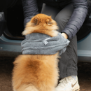 Pomeranian sat outside a car with the door open, dog has it's back to the camera with a person drying the dog with a Henry Wag grey pet glove towel. 