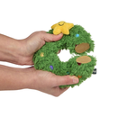 White background with a hand holding a plush dog toy Christmas wreath with a plush star with stitched eyes and smile. The toy is split open to show the rubber internal. 