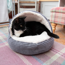Black and white adult cat curled up in a grey cord and cream plush fabric cat cave pictured in a living room environment. 