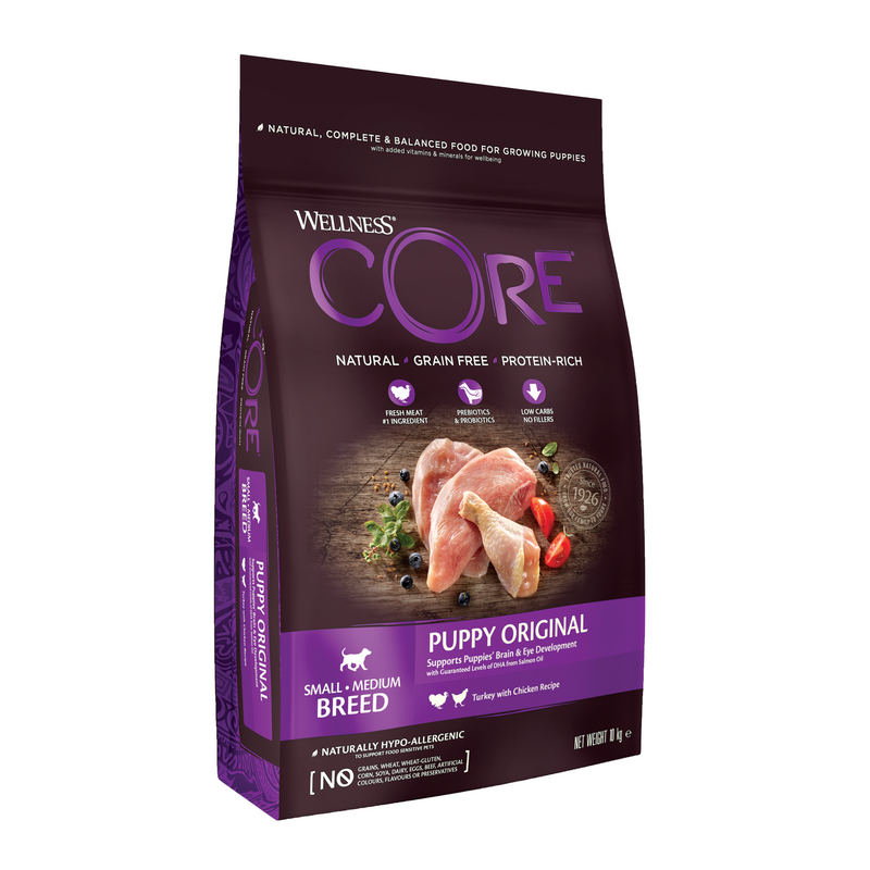 White background with a picture of a bag of Wellness CORE Original Puppy Food. On the bag is pictures of chicken leg, turkey fillet, blueberries and tomatoes. The text on the bag 'Wellness CORE, Natural, Grain Free, Protein-Rich' and 'Small/Medium breed, Puppy Original, Turkey with Chicken Recipe'. 