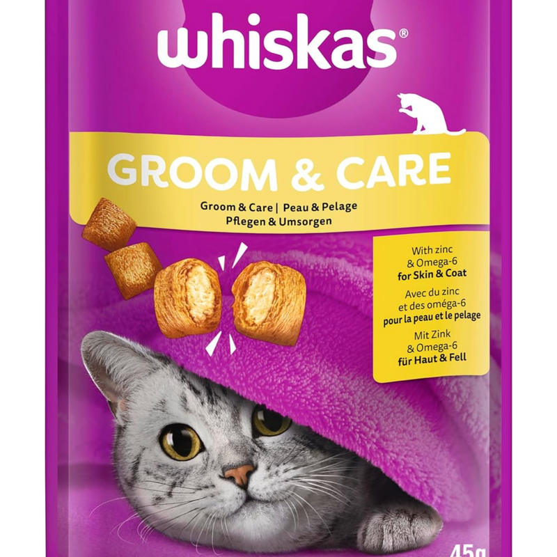 White background with a close up of a purple packet of Whiskas Groom & Care Treats, on the packet is silver tabby cat's face under a purple blanket. Text on the pack reads 'Whiskas Groom & Care, with Zinc & Omega-6 for Skin & Coat.' 