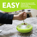 Hand filling the UFO shaped treat dispenser with green central and top parts with main body in grey on a counter top. A bright green banner with white text say 'Easy. Change the level of difficulty to make the puzzles progressively more challenging.' 