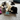 A black and white cat playing with an Ancol plush cat-shaped toy dressed as a bandit with a black-and-white striped shirt and a white bank box, on a living room carpet.