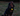 A long-haired black and tan dog sitting on grass at dusk, wearing a red collar with an Ancol glowing yellow acorn-shaped pet lantern attached to the collar.