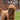 A brown poodle cross dog holding an Ancol Heritage plush bat-shaped dog toy made from brown fabric, in it's mouth. Pictured outside. 
