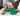 Poodle-cross type dog laying is head on a green Ancol Made From Turtle dog toy, pictured on a cream sofa, with brown cushions.