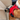 A close-up of a dog wearing a red Ancol Viva exercise & travel harness with black and grey trim, secured with a black buckle, sitting in a beige car seat with the seatbelt fastened.