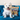 West Highland terrier dog sat on a blue velvet sofa with a stripy cushion behind it. A black and blue bottle of Animology Tear Stain Remover is also on the sofa.