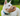 Large white dog wearing a brown basket Baskerville CLASSIC dog muzzle and a blue collar in a garden. 