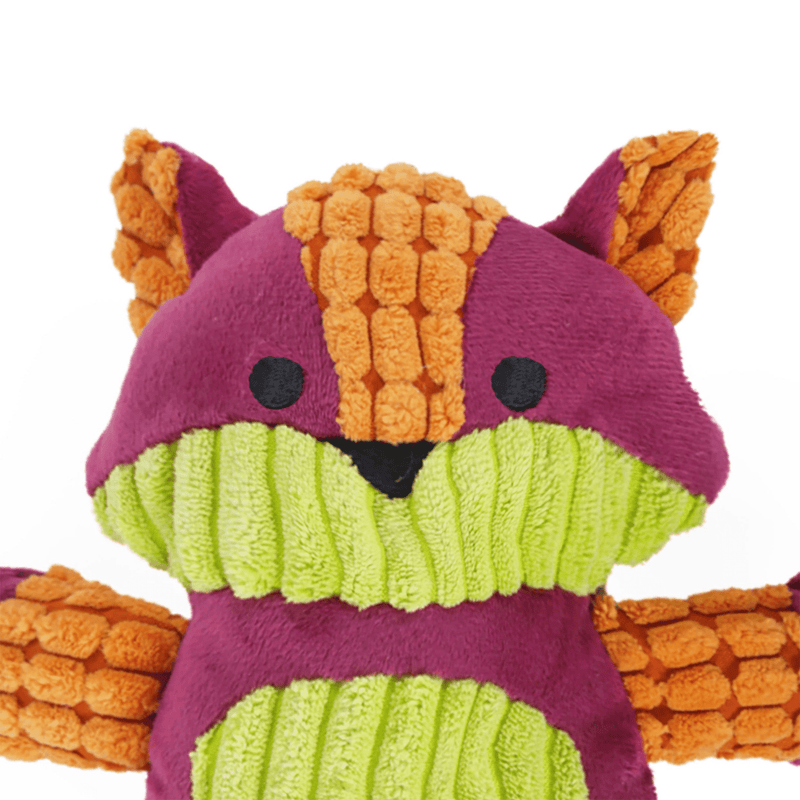 Close up of face of multi-coloured cat shaped dog toy, black stitched eye and nose details, dominantly pink head and body, with orange legs and arms, and pale green chin and belly features on a white background. 
