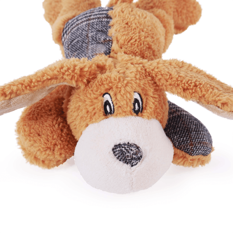 Close up of plush cartoon style dog toy made dominantly from fluffy brown fur with plaid patchwork on one half of the back and one front paw. White muzzle with plaid fabric nose and stitched eye details. Pictured on a white background. 