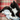 Black and white cat playing with a penguin shaped cat scratcher, dominantly fluffy grey body with a canvas belly, with dark grey beak and feet, with a white pom pom on a string attached pictured on a tartan sofa. 