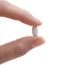 Hand holding a white pill against a white background