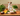 A box of Forthglade adult grain-free turkey dog food, pictured on a table with various vegetables and a bottle of oil. Looking over the table is a Jack Russell terrier.