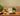 A box of Forthglade Chicken with Liver dry dog food is displayed on a rustic wooden table surrounded by ingredients like sweet potatoes, carrots, parsley, and a bottle of oil, set against a neutral beige background.