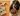 A senior black dog licking diced pieces of wet dog food in a bowl, being held by a person. A packet of Forthglade white fish and brown rice senior dog food is pictured on a kitchen table, next to the dog. 