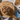 A top-down styled food scene showing cubed brown dog food pieces in a small bowl placed on a round wooden board, with additional slices in a white dish and a blue plate with a knife on a speckled surface.