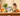 A dog sits at a wooden dining table looking at a box of Forthglade dog food, surrounded by fresh vegetables and ingredients.