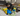 Living room environment with a black and tan small dog with two blue and yellow Happy Pet Minion dog toy with tug ropes at the top and bottom, one large and one small.