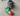 A grey dog laying on a beige carpet playing with a colourful Happy Pet Very Hungry Caterpillar plush dog toy.
