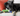 Black mixed breed dog with a KONG Shakers Cuckoo duck dog toy, with a long green neck and blue body, yellow beak and legs with stitched features.