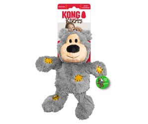 White background with a KONG grey plush teddy bear dog toy with yellow patchwork patches attached to a cardboard backing.