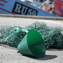 Harbour scene with a boat visible in the background, in the foreground is a green Elizabethan style recovery collar with a green fishing net behind it. 
